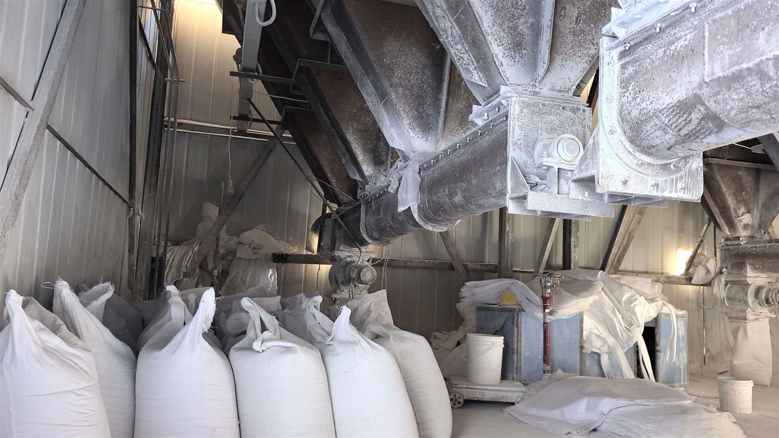 Inside the white zircon silica fume production workshop, 25kg bags stacked, conveyor pipes above